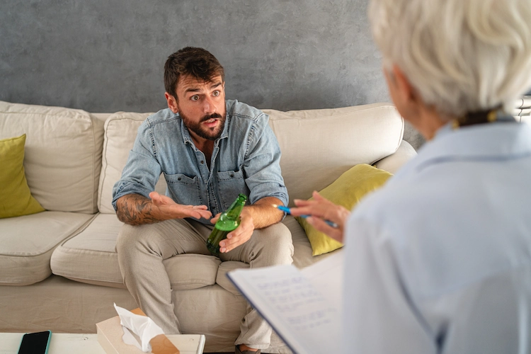 a man with a bottle of beer speaking to a therapist looking angry
